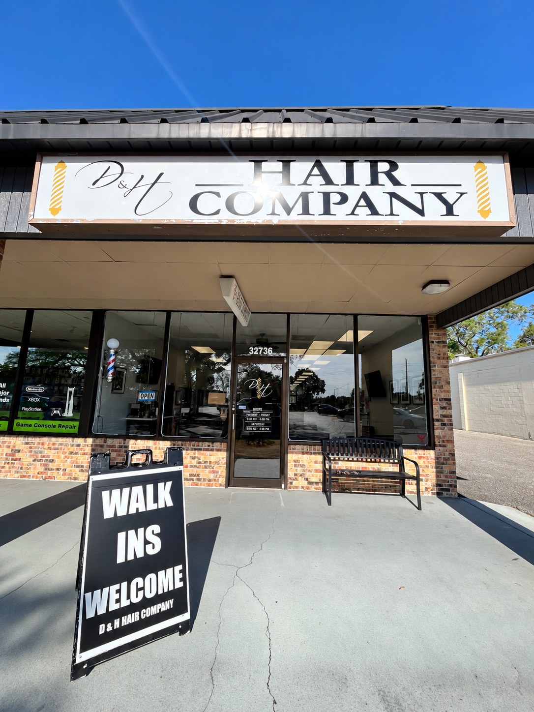 The D&H Hair Company storefront with its sign, the 32736 glass entrance door, and a Walk Ins Welcome A-frame sign on the sidewalk