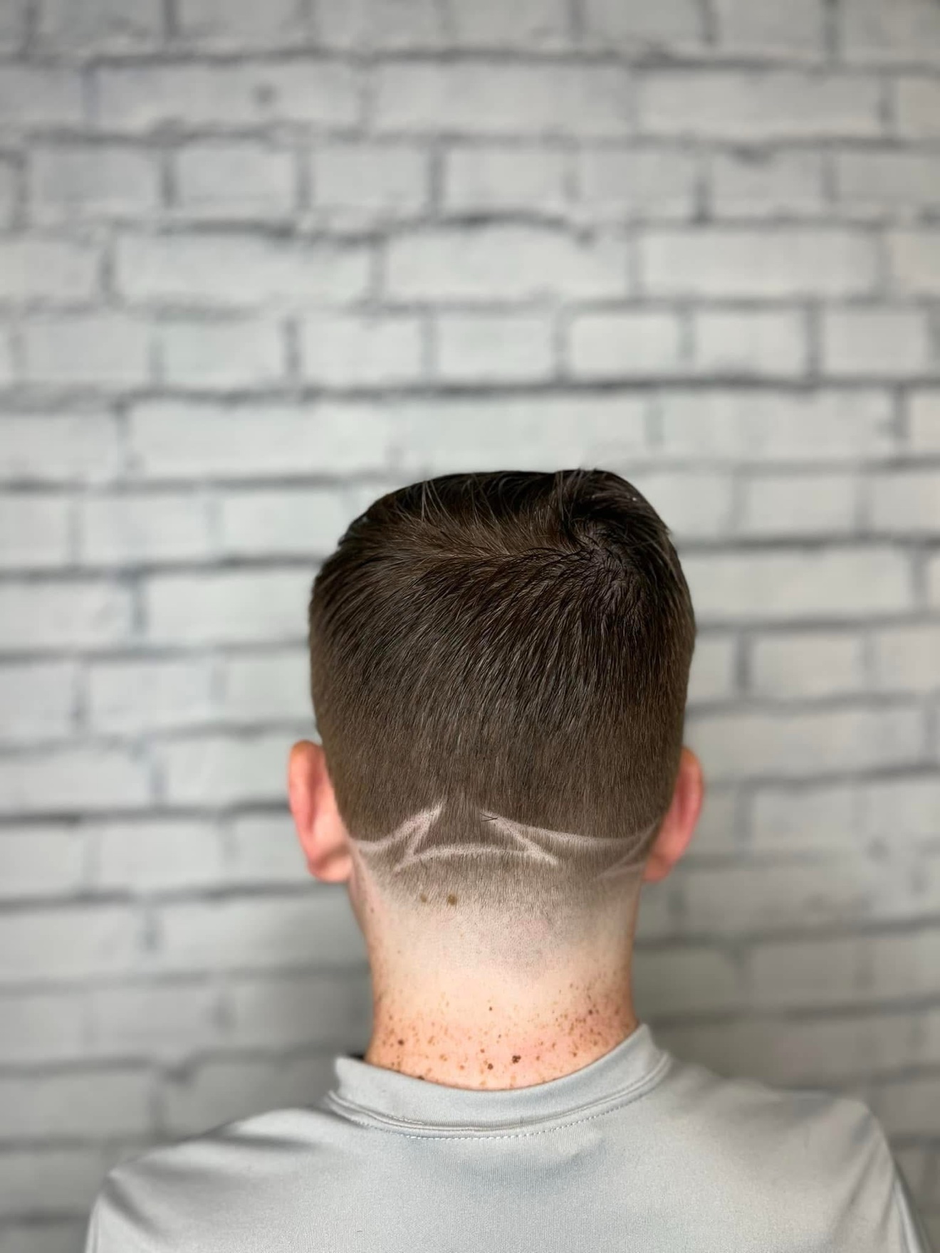 Taper fade with a lightning bolt design at the nape, back view, by Danny at D&H Hair Company