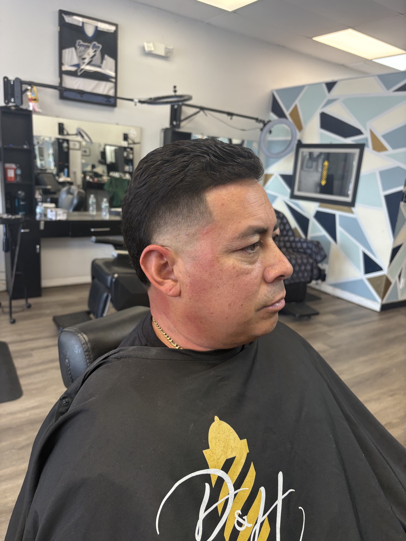 Taper fade with a side-swept top, client wearing a D&H Hair Company cape, side view, by Danny