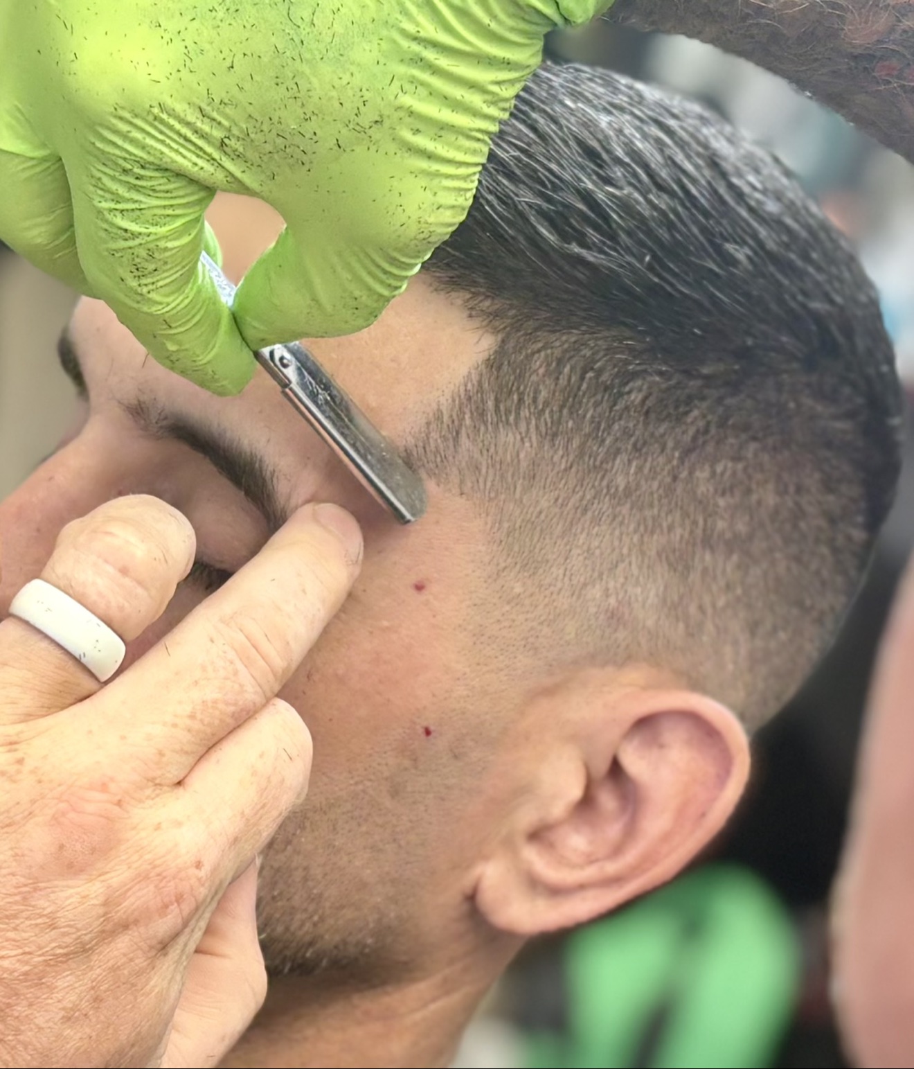 Close-up of a straight-razor temple lineup, green-gloved hand at work, by Danny at D&H Hair Company