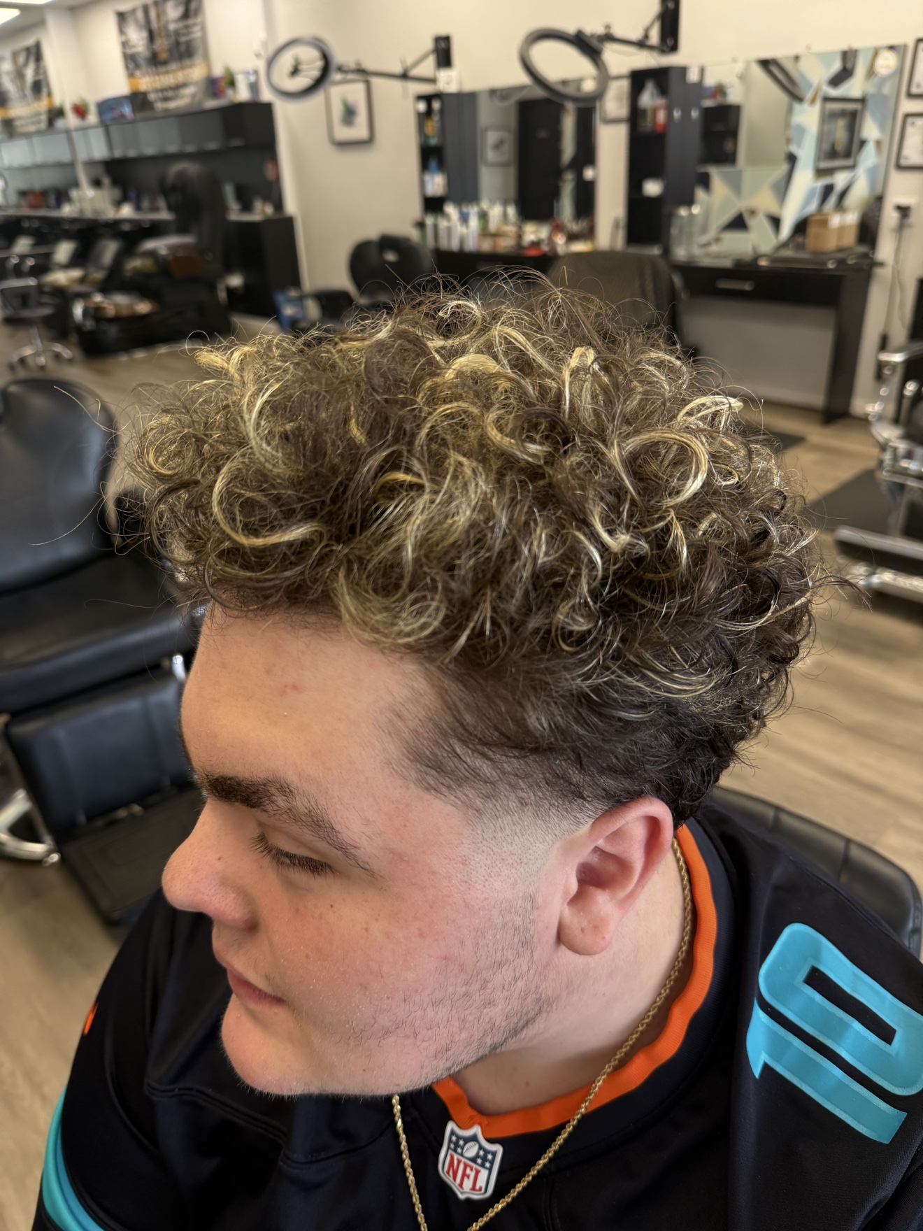 Curly hair with blonde highlights and a fade, side view, by Heather at D&H Hair Company